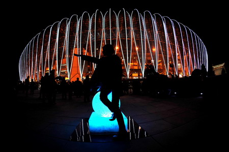 An audience poses for photos with the Jinan Olympic Sports Center Stadium in the background before the opening ceremony of the 11th National Games held in Jinan, Shandong Province Oct 16, 2009. [Xinhua]