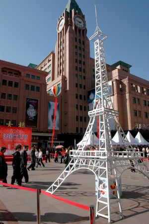 Several passers-by glimpse at the mimic model of the Eiffel Tower on display during the 2009 French Cultural Festival slated from October 10th to 18th, on the Wangfujing Street, in downtown Beijing, Oct. 17, 2009.[Li Wenming/Xinhua]