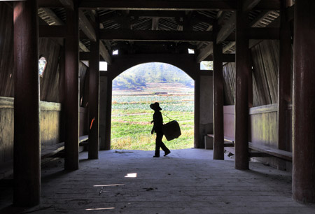 A local resident walks on Guangli Bridge, a roofed wooden arch birdge, in Pingnan County of southeast China's Fujian Province, Oct. 17, 2009. [Jiang Kehong/Xinhua]