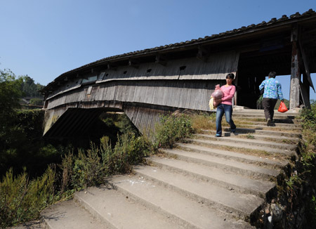 Local villagers walk past Guangfu Bridge, a roofed wooden arch birdge, in Pingnan County of southeast China's Fujian Province, Oct. 17, 2009. [Jiang Kehong/Xinhua]