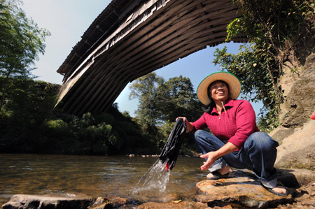 A local villager wash clothes with the backdrop of Guangfu Bridge, a roofed wooden arch birdge, in Pingnan County of southeast China's Fujian Province, Oct. 17, 2009. [Jiang Kehong/Xinhua]