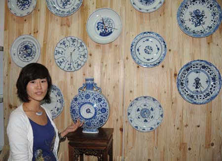 A woman shows blue-and-white porcelain clocks at the exhibition hall of 2009 China Jingdezhen International Ceramic Fair in Jingdezhen, east China's Jiangxi Province, Oct. 18, 2009. The 2009 China Jingdezhen International Ceramic Fair kicked off here on Oct. 18. [Shi Weiming/Xinhua]