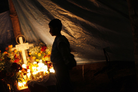 A child stands next to the grave of a child at the cemetery in Tzintzuntzan, Mexico October 31, 2009. Mexicans pay homage to their dead relatives by preparing meals and decorating the graves on the first two days of November. The Day of the Dead festival has its origins in a pre-Hispanic Aztec belief that the dead return to Earth one day each year to visit their loved ones.