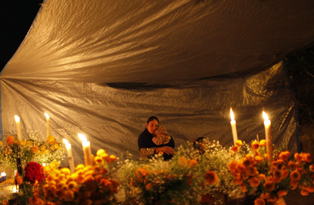 A woman holds a baby while sitting next to the grave of a child at the cemetery in Tzintzuntzan, Mexico October 31, 2009.