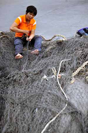 A Fisherman repairs fishing net in a port in Haikou, capital of south China's Hainan Province, Nov. 2, 2009. [Guo Cheng/Xinhua] 