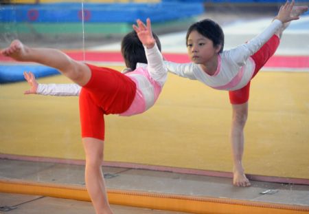 Yang Le, a 6-year-old girl practises basic gymnastics skills in front of the mirror in a gymnastics school of Xiantao, city of central China's Hubei Province, on Oct. 15, 2009.(Xinhua/Li Xiaoguo)