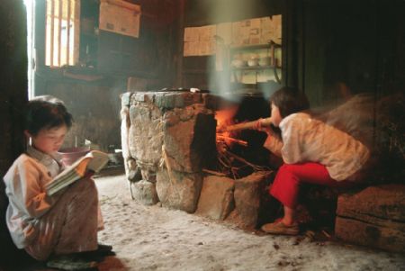 Zheng Meihua (R) cooks supper while her sister Zheng Meitao reads her textbook after school in Taishun County, Zhejiang Province in this photo taken in April, 1994. The sisters went back to school with the help of Hope Project after suffering the death of their parents.(Xinhua Photo)