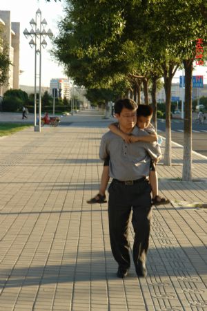 Liu Hao, an eight-year-old blind boy of a worker's family, is carried on the back of his piano teacher Liu Yongxue en route to piano room for practice, in Chifeng City, north China's Inner Mongolia Autonomous Region, July 9, 2009. [Xinhua]