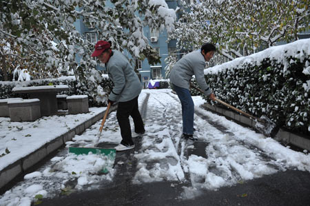 People clean up snow on a road in the Yicuiyuan community in Beijing, capital of China, Nov. 10, 2009. Beijing witnessed the second snowfall this winter on Nov. 10.[Xinhua]