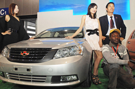 Visitors pose for photos in front of a Geely Emgrand EC718 vehicle during the 2009 China International Tourism Commodities Fair in Yiwu city of east China&apos;s Zhejiang Province, Nov. 12, 2009. Some 60,000 exhibitors attended the fair which runs from Nov. 12 to 15. [Tan Jin/Xinhua]