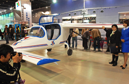 A visitor (2nd, R) poses for photo in front of a China-made ultralight plane during the 2009 China International Tourism Commodities Fair in Yiwu city of east China&apos;s Zhejiang Province, Nov. 12, 2009. Some 60,000 exhibitors attended the fair which runs from Nov. 12 to 15. [Tan Jin/Xinhua]