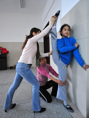 Deaf-mute student Liu Yidan (R) stretches her leg with the assistance of a classmate and her teacher Feng Yan (L) during a dance class at a special education school in Yichang City, Central China&apos;s Hubei province, November 19, 2009.[Xinhua]