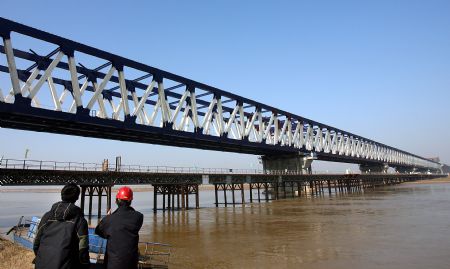 Two men look at the alomost-finished Zhengzhou Yellow River highway and railway dual-use bridge in central China's Henan Province, on Nov. 22, 2009. The bridge is expected to be completed in July 2010 and open to traffic in the end of October 2010. The bridge, connecting Zhengzhou and Xinxiang of Henan Province, serves as the longest (9,177 meters) huge-sized highway and railway dual-use bridge over the Yellow River, with the highest designed railway speed of 350 kilometers per hour. (Xinhua/Wang Song)