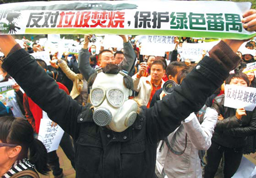 A masked protester makes a point as more than 1,000 residents demonstrate outside the Guangzhou government building yesterday. The sign reads: “Oppose garbage burning, protect green Panyu.” [China Daily]  