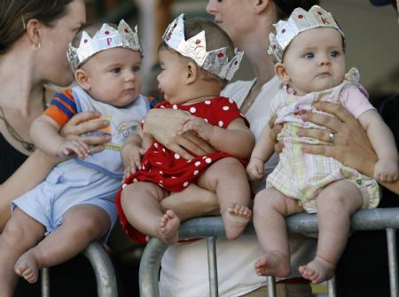 Six-month-olds Philip Hanekom (L), Sadie Jimenez (C), and Kyla White sporting homemade crowns are held by family friends as they wait for Britain's Queen Elizabeth and Prince Phillip at King's Square, St. George's in Bermuda November 24, 2009. The queen's three-day visit commemorates the 400th anniversary of the island.