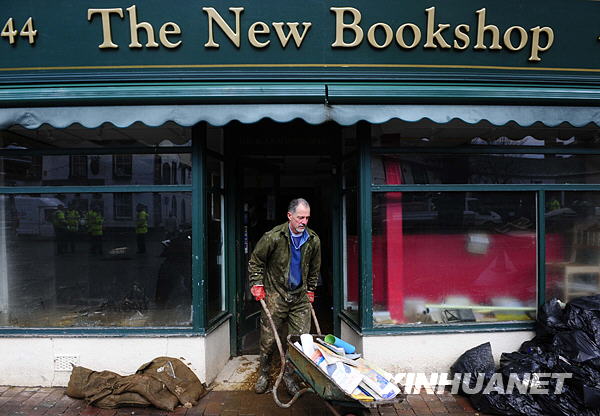 A man carries books dipped in flood from a bookstore in Cockermouth, northwest England, Nov. 26, 2009. The British Environment Agency has announced that only one flood warning remains in force in Cumbria, a week after unprecedented rainfall prompted some of the country&apos;s worst ever flooding, while Cumbria County Council has said that 21 road bridges are still closed. [Zeng Yi/Xinhua]