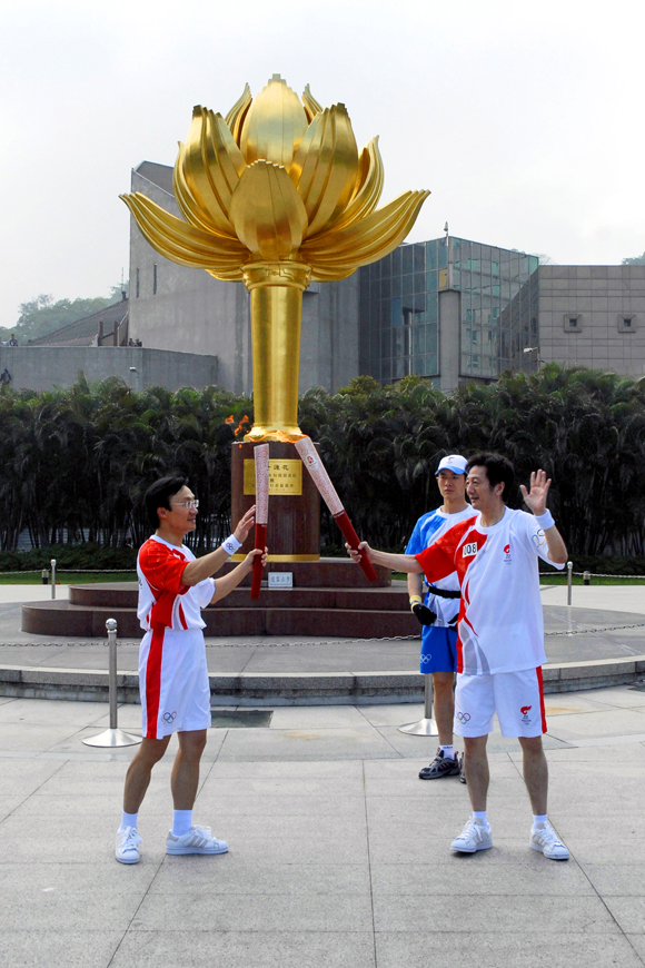 A torch bearer successfully lights a flame pot that was handed over by another torch bearer at Golden Lotus Square in Macao.