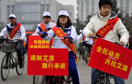 College volunteers carrying posters urging for a concerted effort to battle AIDS ride bikes on a street for an AIDS-awareness event in Huhhot, capital of north China&apos;s Inner Mongolia Autonomous Region, Dec. 1, 2009, World AIDS Day. (Xinhua/Ren Junchuan)