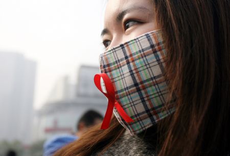 A girl pastes a red ribbon on the mask during an AIDS awareness activity held at the Shanghai Railway Station by Zhabei District Center for Disease Control & Prevention in Shanghai, east China, Dec. 1, 2009. (Xinhua)