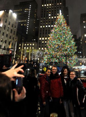 Tourists pose for a photo in front of the shining Christmas tree at the Rockefeller Center in New York, the United States, Dec. 2, 2009. The 76-feet-tall Christmas tree was illuminated Wednesday, which was decorated with 30,000 colorful lights.