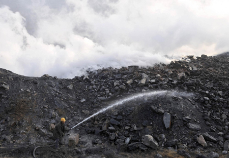 A miner sprays water on coal to prevent dust from settling at the Haizhou open-cast coal mine in Fuxin, Liaoning province November 22, 2009. Fuxin, in China's northeast Liaoning Province, which relied mainly on mining in the past, is the first pilot city identified by the State Council to transform its economy, Xinhua News Agency reported.