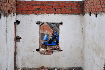 A resettler drives a tricycle past the dismantled house in Junxian County, Danjiangkou City of central China&apos;s Hubei Province December 8, 2009. [Xinhua]