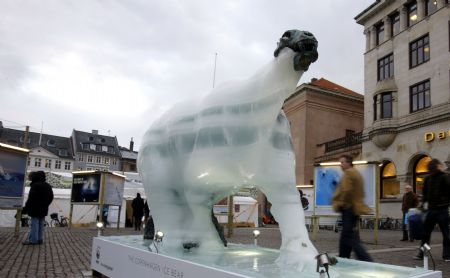 People pass by an ice sculpture of a polar bear as it melts to reveal a bronze skeleton in Copenhagen Dec. 8, 2009. [Xinhua]