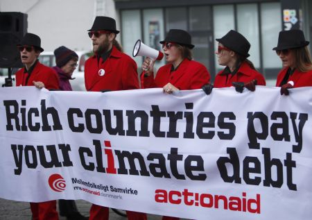 Members of environmental activist group Act!onaid, dressed as &apos;climate debt agents&apos;, hold up a banner outside the congress centre, before the opening of the United Nations Climate Change Conference 2009 in Copenhagen December 7, 2009.[Xinhua/Reuters]