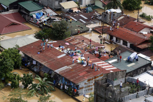 People wait for rescue on the top of their submerged houses in Cainta of Rizal Province, the Philippines, on Sept. 27, 2009. At least 51 people were killed while 21 others remain missing as tropical storm Kestana hit the Philippines and brought massive flood on Saturday, the government disasters relief agency said Sunday. (Xinhua/Stringer)