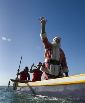 A man dressed as Santa Claus waves to the crowd on Waikiki beach as he arrives in an outrigger canoe in Honolulu, Hawaii December12, 2009.