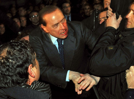 Italian Prime Minister Silvio Berlusconi (C) reacts after being assaulted in Milan. Berlusconi was rushed to hospital after a man with a history of mental problems attacked him, knocking out two of his teeth, following a political rally in Milan Sunday. [Xinhua/AFP]