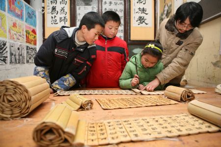 A teacher (R) guides pupils practising Chinese calligraphy works on Chinese traditional bamboo slips at the Sunny Future Primary School in Xiangfan, central China&apos;s Hubei Province, Dec. 14, 2009. [Gong Bo/Xinhua]