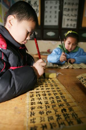 Two pupils practise Chinese calligraphy works on Chinese traditional bamboo slips at the Sunny Future Primary School in Xiangfan, central China&apos;s Hubei Province, Dec. 14, 2009. [Gong Bo/Xinhua]