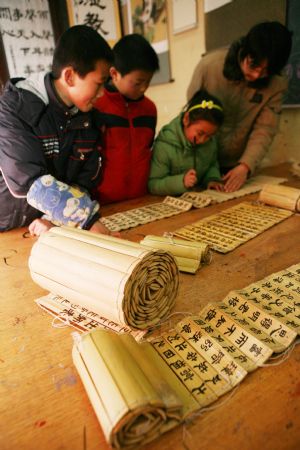 A teacher guides pupils practising Chinese calligraphy works on Chinese traditional bamboo slips at the Sunny Future Primary School in Xiangfan, central China&apos;s Hubei Province, Dec. 14, 2009. [Gong Bo/Xinhua]