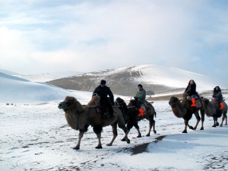 Tourists on camel back pass the snow covered Mingshashan in Dunhuang, northwest China&apos;s Gansu Province Dec. 14, 2009. [Zhang Weixian/Xinhua]