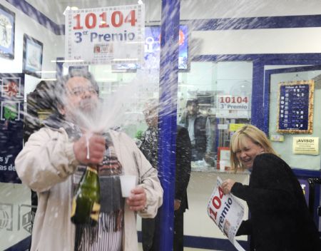 Lottery salesman Gonzalo Menendez sprays champagne next to his daughter at their lottery shop where he sold part of the number awarded with the third prize of El Gordo, Spain&apos;s Christmas lottery in Corvera, northern Spain, December 22, 2009.(Xinhua/Reuters Photo)