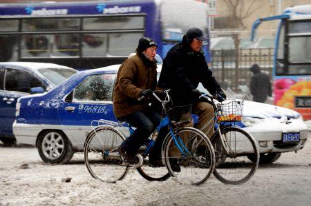 Citizens ride on snow-covered street in Shenyang, capital of northeast China's Liaoning Province, Dec. 25, 2009. A strong cold wave and heavy snowfall hit Liaoning Province from Thursday night, causing a sudden temperature fall of over ten degrees Celsius. [Zhang Wenkui/Xinhua]