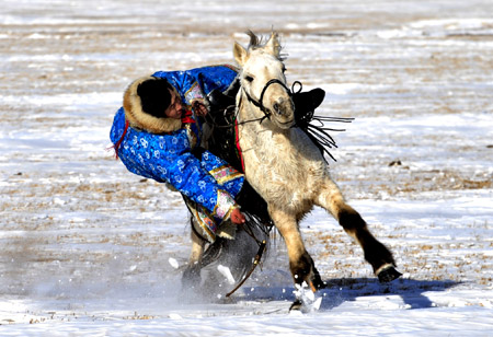 A herdsman tries to pick a thing on a running horse in Xi Ujimqin Qi, north China's Inner Mongolia Autonomous Region, on Dec. 28, 2009. (Xinhua/Ren Junchuan)