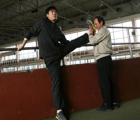 Liu Xiang (L), athlete of men's 110 metres hurdles race, raises leg in cooperating with his trainer Sun Haiping during the first open winter training session of the China's national team of track and field, at the Xingzhuang Training Base, in Shanghai, east China, on Dec. 29, 2009. (Xinhua/Fan Xiaoming)