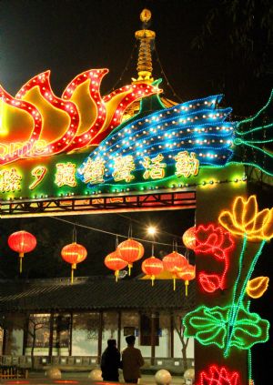 Two visitors walk past the avenue of the Fengqiao (Maple) Bridge of the Hanshan Temple which are illuminated and festooned with lanterns and colored streamers, in Suzhou, east China&apos;s Jiangsu Province, Dec. 29, 2009.[Wang Jianzhong/Xinhua]