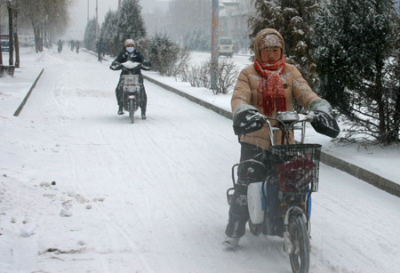 People ride electric bicycles in the street during a snowfall in Hohhot, north China's Inner Mongolia Autonomous Region, Jan. 3, 2010. China's Central Meteorological Station (CMS) on Sunday morning extended the warning against strong cold wave, snowstorm and heavy fog by issuing another orange alert.(Xinhua/Li Yunping)