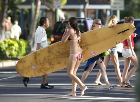 A surfer crosses a street past tourists on Waikiki Beach in Honolulu, Hawaii, January 2, 2010.(Xinhua/Reuters Photo)