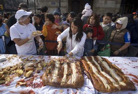 A woman cuts the traditional &apos;Rosca de Reyes&apos; baked for Epiphany in Mexico City, capital of Mexico, on Jan. 3, 2010. The biggest &apos;Rosca de Reyes&apos; of the world, of 720 meters length and 12,000 kg weight, was distributed to 250,000 people at the Zocalo square in Mexico City. [Xinhua]