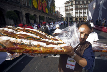 A man carries a piece of traditional &apos;Rosca de Reyes&apos; baked for Epiphany in Mexico City, capital of Mexico, on Jan. 3, 2010. The biggest &apos;Rosca de Reyes&apos; of the world, of 720 meters length and 12,000 kg weight, was distributed to 250,000 people at the Zocalo square in Mexico City. [Xinhua]