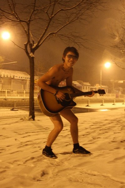 A young boy wearing shorts poses for photograph in the snow late at night on Ping&apos;an avenue, Beijing. [peopledaily.com.cn]