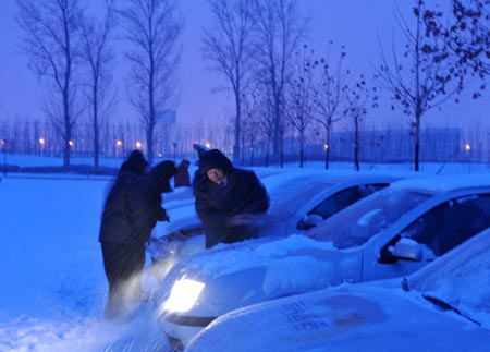 People clean the snow-covered vehicles during a heavy snowfall at Daxing district in Beijing, China, Jan. 3, 2010.[Xinhua]