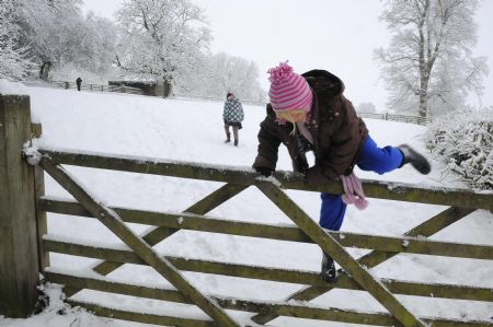 A girl climbs a gate in a snow covered field in Helperby, northern England January 5, 2010. Freezing conditions and heavy snowfall brought more chaos to the transport network on Tuesday, shutting airports and disrupting train services. [Xinhua/Reuters]