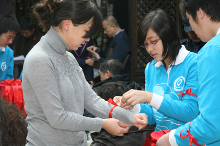 Volunteers tie red ribbon for a participant of the launch ceremony. [China.org.cn]