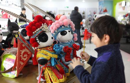 A boy is attracted by the cute Panda dolls in Peking Opera&apos;s makeup style, a novel doll brand series of Panda Town wrought by a group of young designers born after 1980s who returned to China after having finished education overseas, which is in limelight at a doll shop in Beijing, Jan. 10, 2010. [Luo Wei/Xinhua]