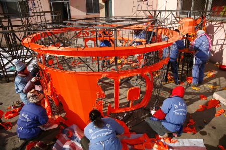 Folk craftsmen decorate a large lantern at a handicraft factory in Rushan, east China's Shandong Province, Jan. 14, 2010. A total of 38 sets of lanterns, fixing the LED light bulbs for energy saving, were under-making here for the local Spring Festival lantern fair this year.(Xinhua/Liu Guoxian)
